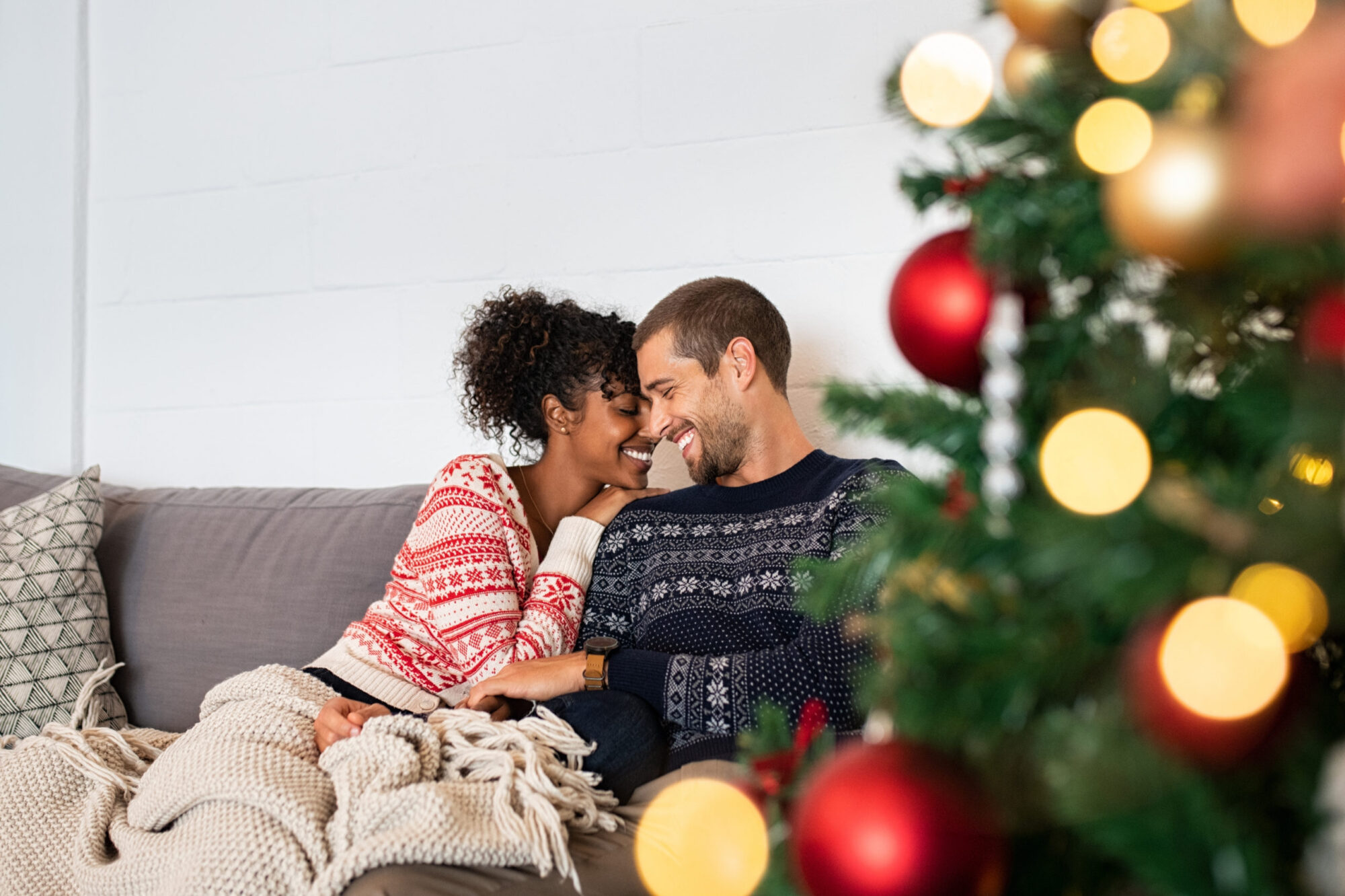 Young happy couple sitting in front of a Christmas tree.