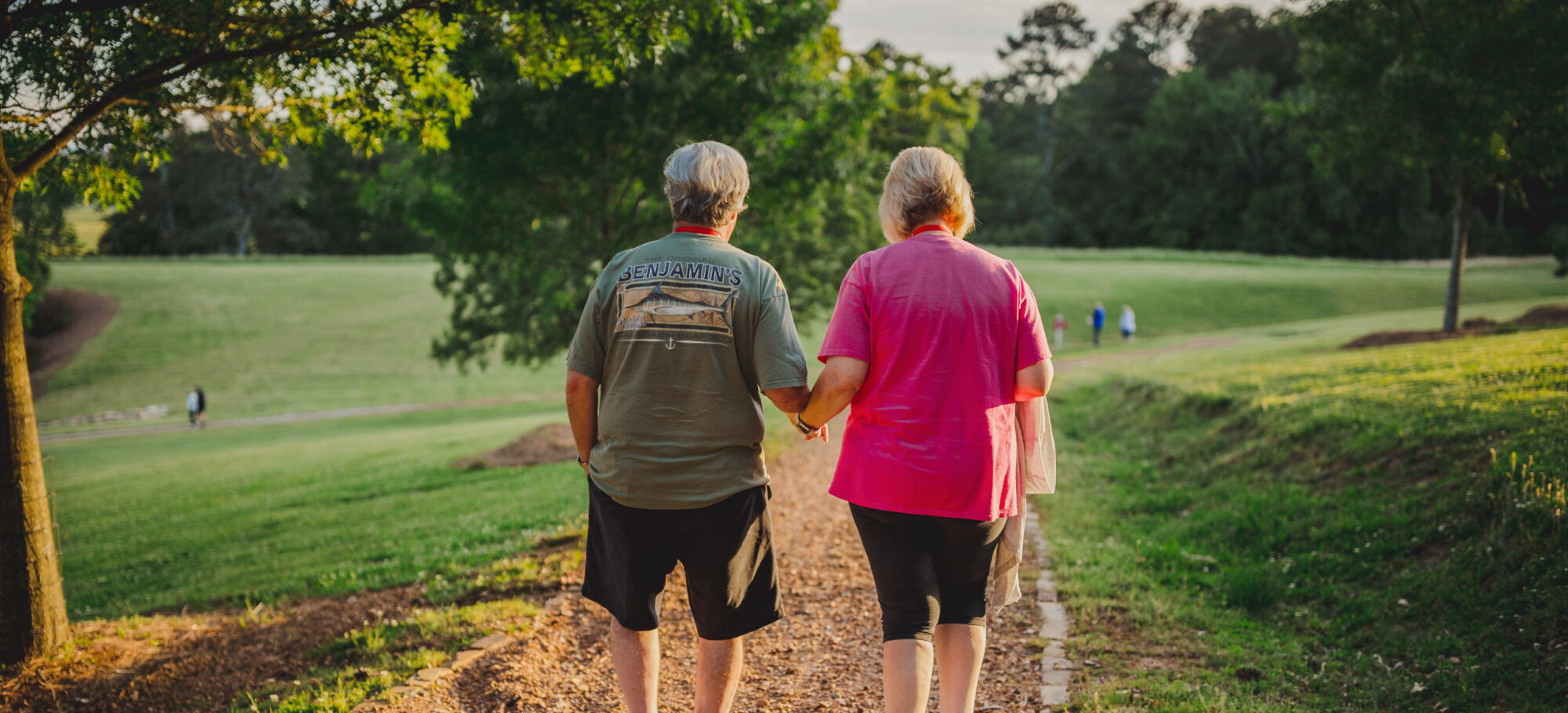 A couple holding hands while walking through a green field at a WinShape Marriage Retreat.