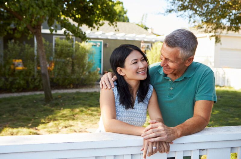 Empty Nest Couple smiling while leaning against a fence