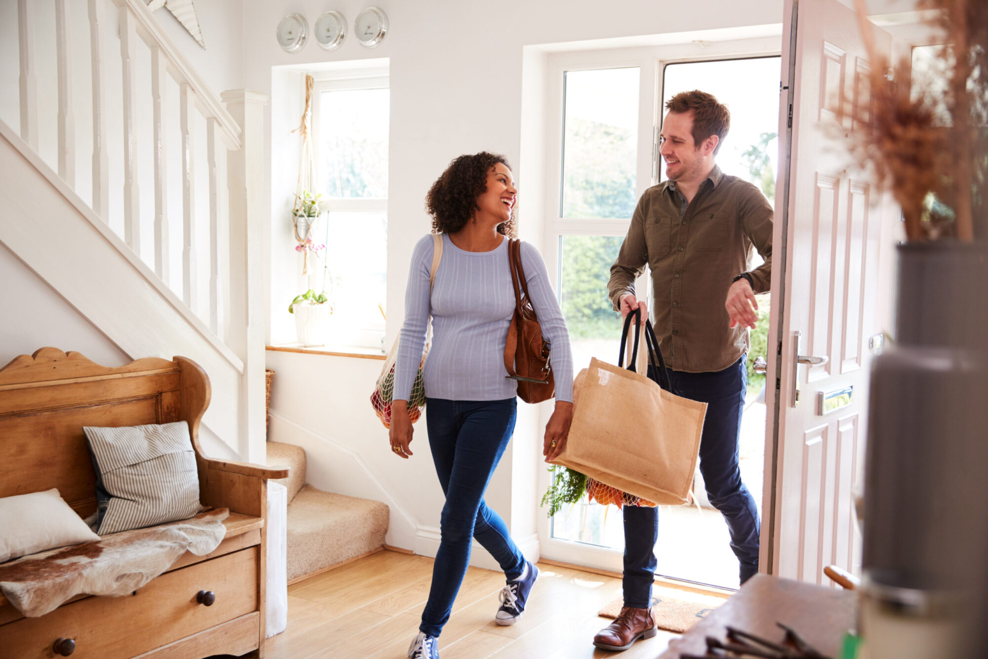 Married Couple Returning Home From Shopping Trip Carrying Groceries In Plastic Free Bags