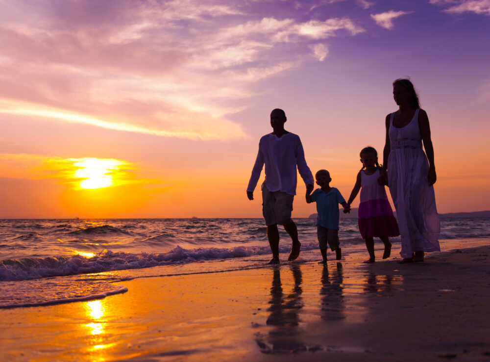 Young married couple with children enjoy a summer date walking the beach at sunset one of our summer date ideas