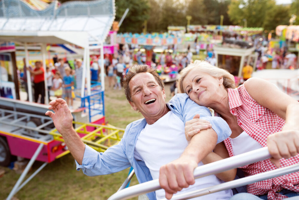 Older married couple laughing while riding a ride at a fall fair together on an autumn date