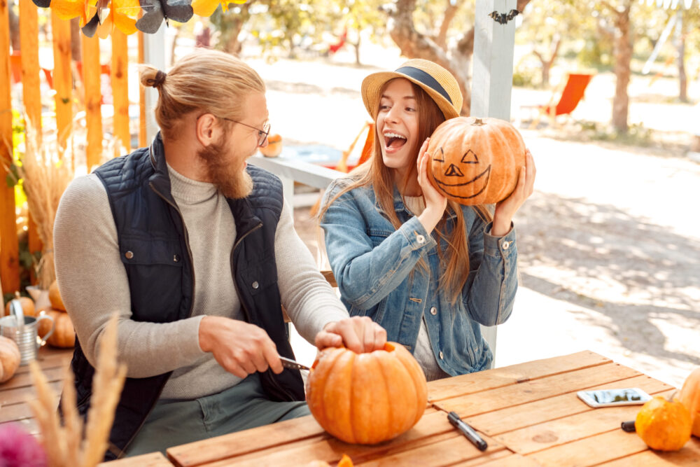 Young married couple enjoying a fall date painting and carving pumpkins together