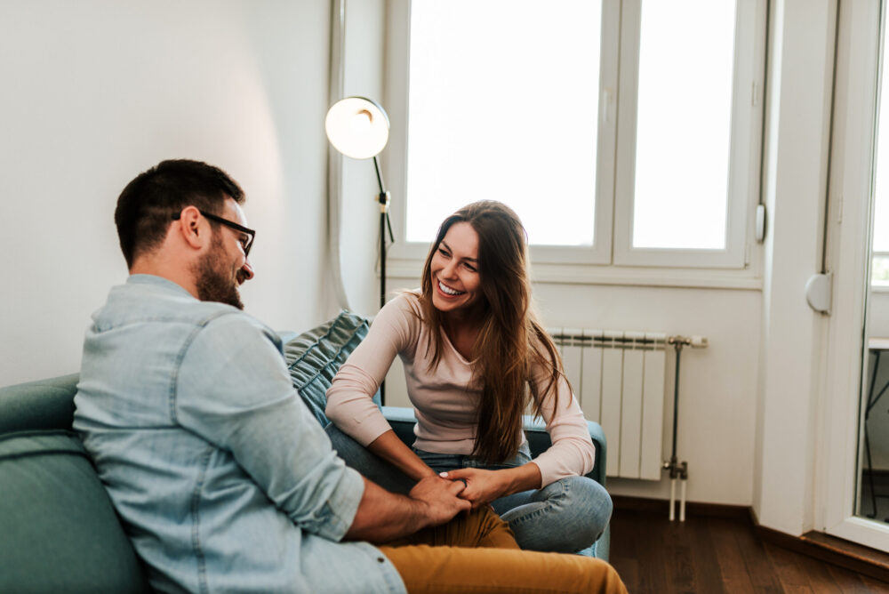 Younger married couple connecting on the couch after being apart for the day; they're working on implementing our tips for how to communicate better with your spouse