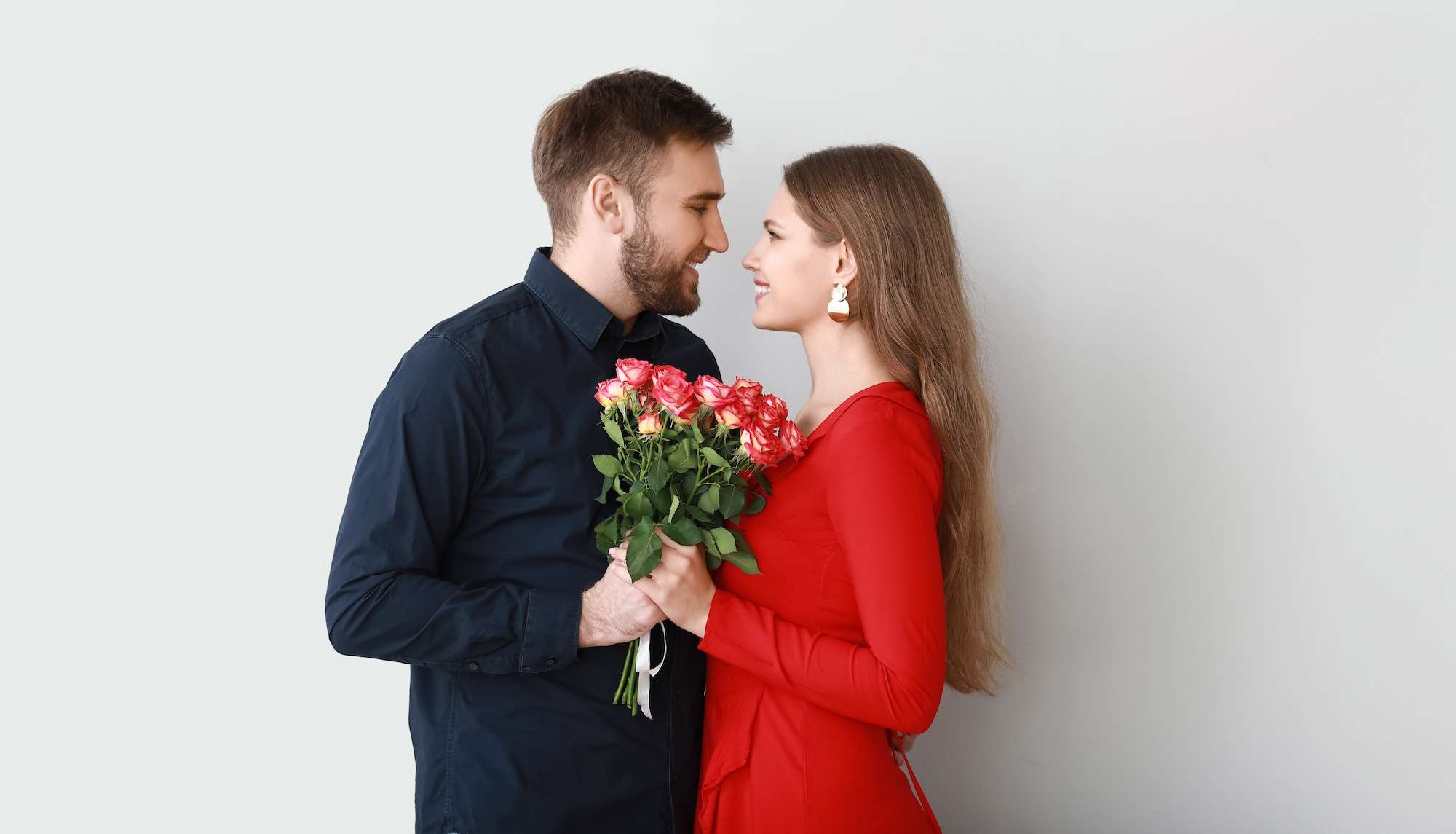 Happy young couple with flowers on light background