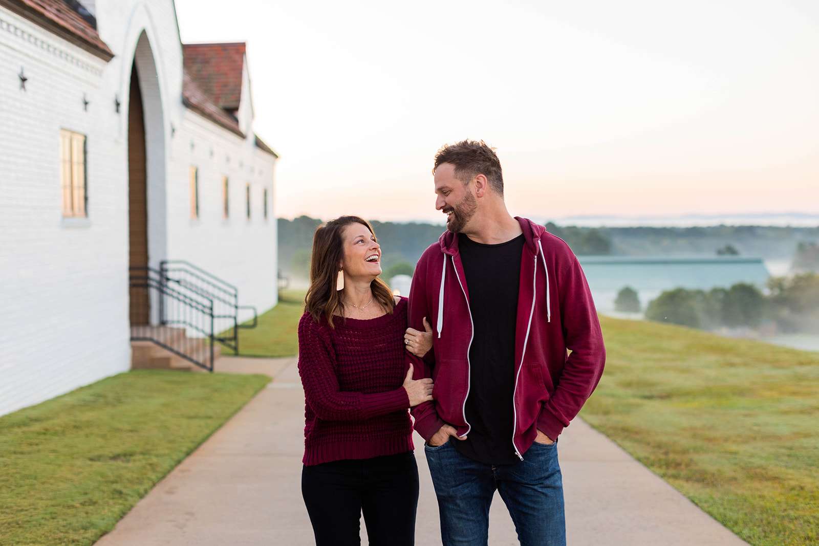 couple embracing and laughing while walking around winshape retreat, white building in background