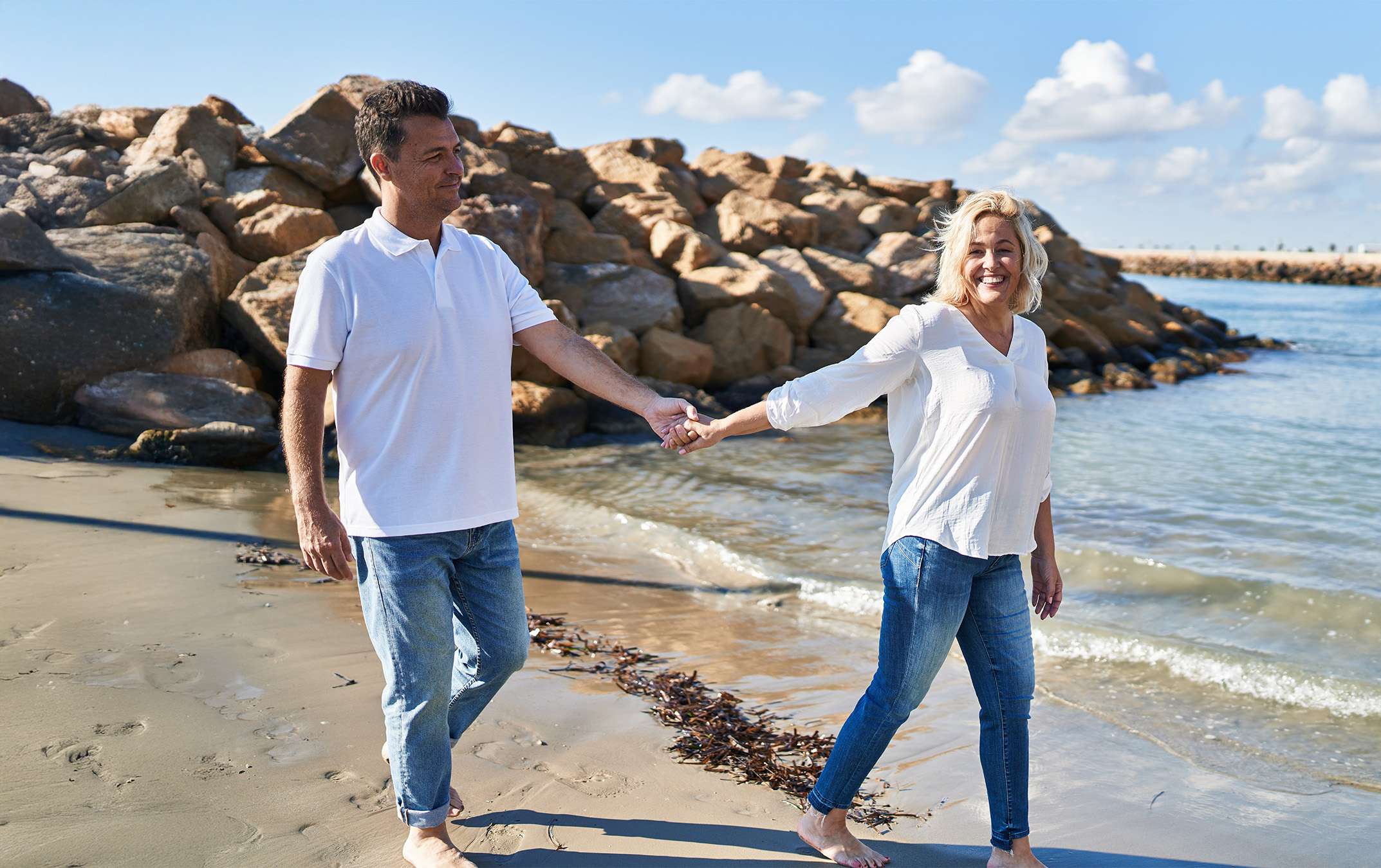happy couple smiling while walking barefoot on the beach