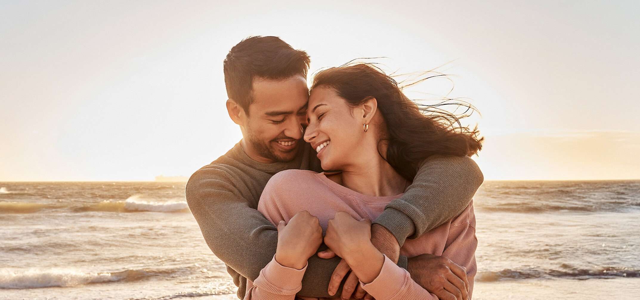couple smiling and embracing at sunset at the beach