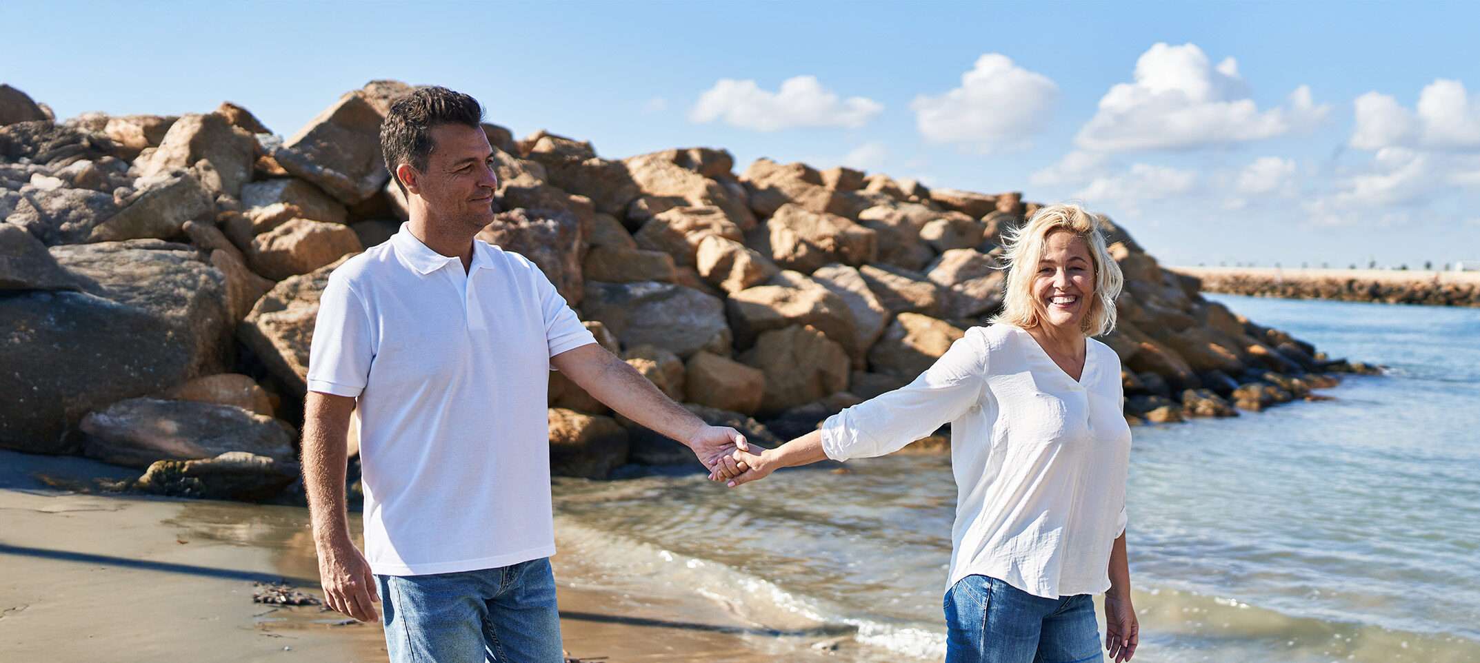happy couple smiling while walking barefoot on the beach